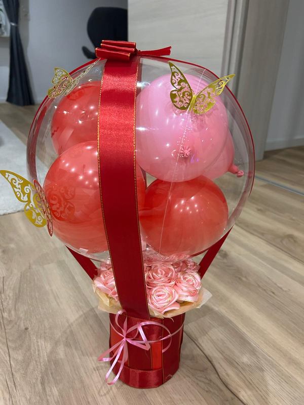Transparenter Bubble-Ballon mit roten und rosa Ballons, Sockel aus rosa Satinrosen und goldenen Schmetterlingen