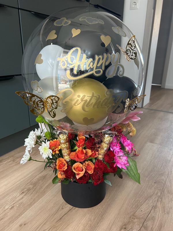 Happy-Birthday-Bubble-Ballon in Gold und Schwarz auf einer Box mit frischen Rosen und Chrysanthemen