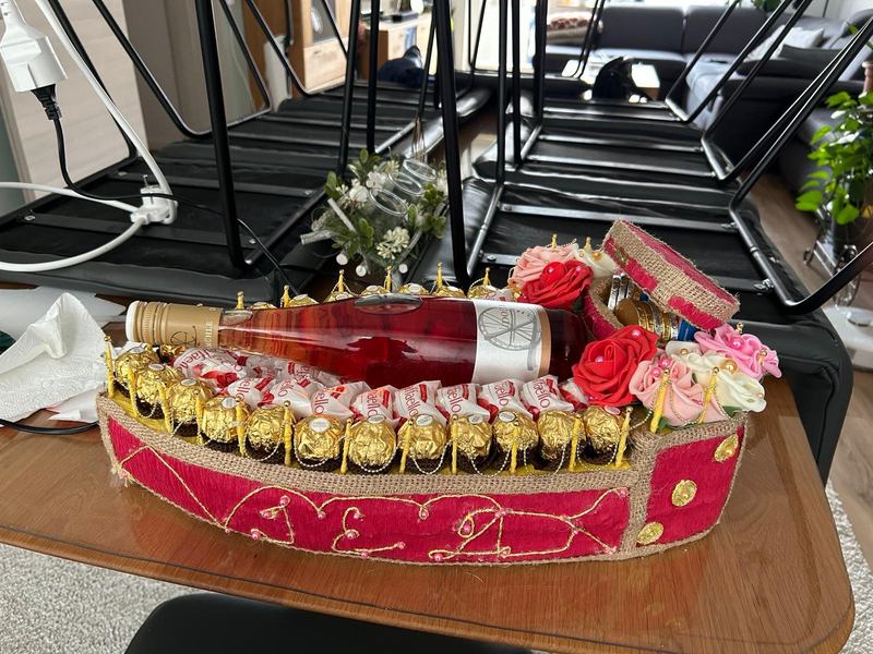 Geschenkschiff aus Jute und rotem Stoff mit Weinflasche, Ferrero Rocher, Raffaello und Seifenrosen
