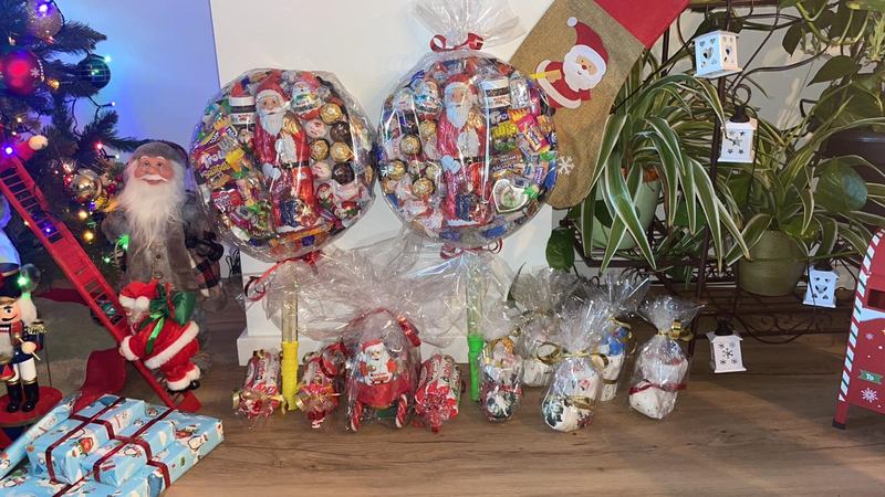 Weihnachtliche Süßigkeitenkugeln, kleine Schlitten und Nikolaus-Tüten vor geschmücktem Christbaum